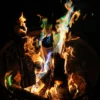 Firelight Ritual Gallery Image | Meriem Chrrouhi Gold and blue-green flames rising from logs in a dark metal fire basket.