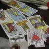 Tarot spread with The Star, Three of Swords and other cards beside beads and rose petals on a dark table.