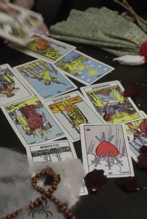 Tarot spread with The Star, Three of Swords and other cards beside beads and rose petals on a dark table.
