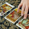 Hand resting beside The Empress, The World and Ten of Pentacles tarot cards on patterned fabric.